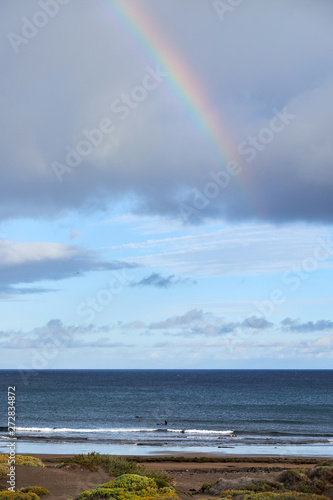 Rainbow over the ocean. Rainbow over the sea. Waves crashing on shoreline.