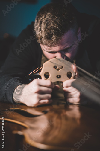 Young luthier working in his workshop, building a double bass photo