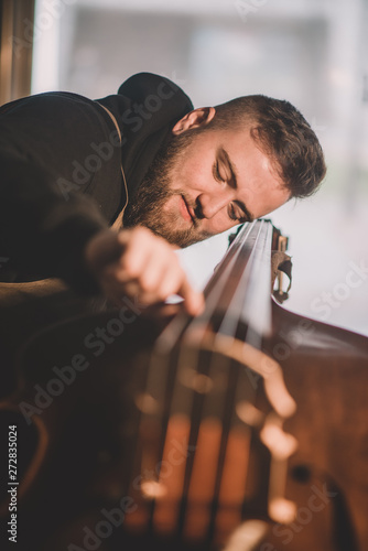 Young luthier working in his workshop, building a double bass