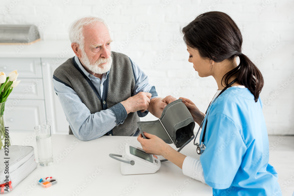Fototapeta premium Nurse measuring blood pressure of bearded grey haired man