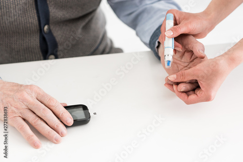 Cropped view of woman hands measuring blood sugar of senior man