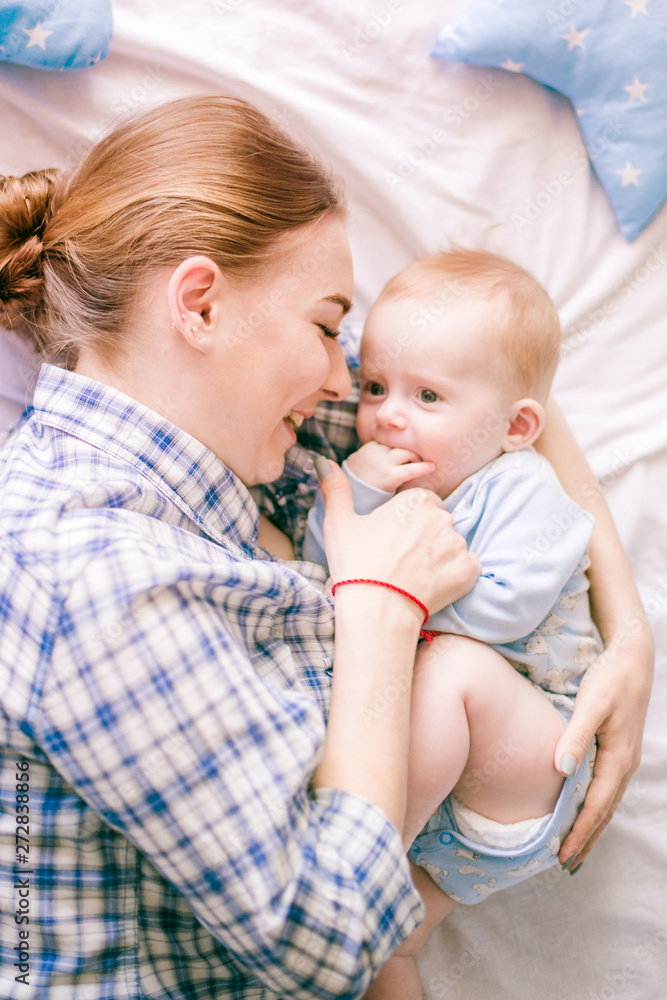 Portrait of beautiful mom in shirt and blue jeans playing with her baby boy in bedroom Portrait of beautiful mom in shirt and blue jeans playing with her baby boy in bedroom