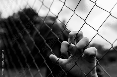 Young unidentifiable teenage boy holding the wired garden at the correctional institute in black and white, conceptual image of juvenile delinquency, focus on the boys hand.