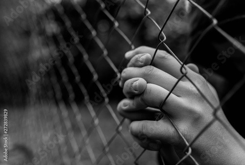 Papier peint Young unidentifiable teenage boy holding the wired garden  praying at the correctional institute in black and white, conceptual image of juvenile delinquency, focus on the boys hand