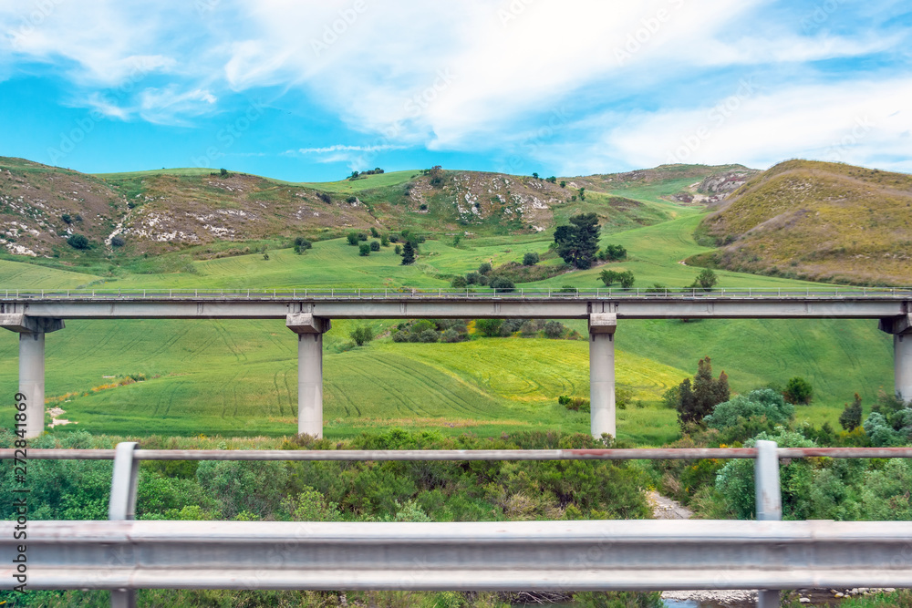 Road highway bridge, viaduct supports in the valley among the green hills, transport infrastructure.