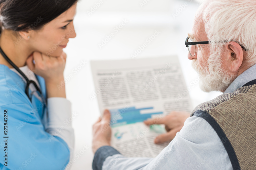 Obraz premium Selective focus of grey haired man talking with nurse, holding newspaper in hands