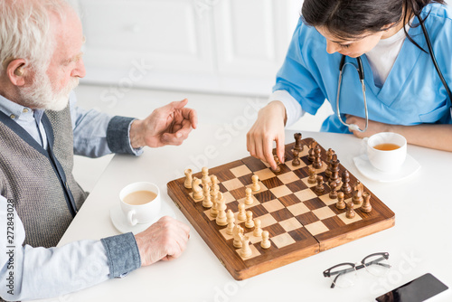 High angle view of nurse with senior man sitting on kitchen, playing in chess