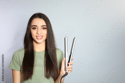 Happy woman with hair iron on grey background. Space for text