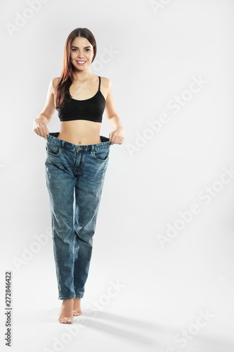Attractive young woman with slim body wearing her old big jeans on white background. Space for text