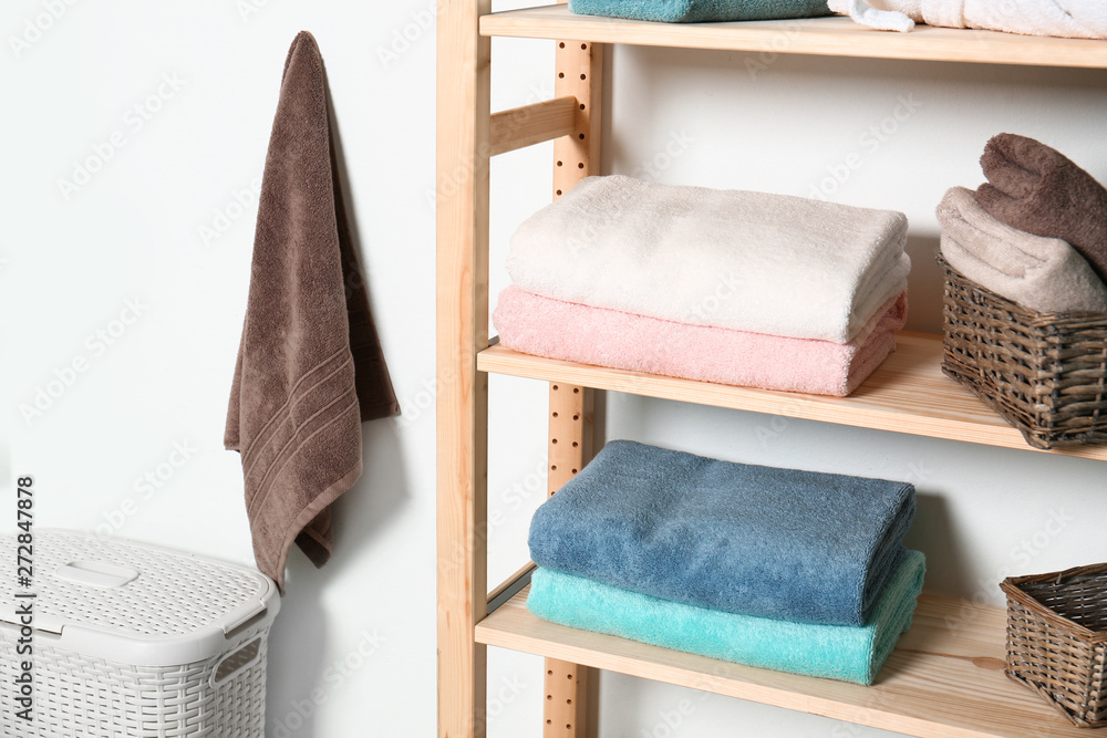 Shelving unit with clean towels near white wall in modern bathroom interior Shelving unit with clean towels near white wall in modern bathroom interior