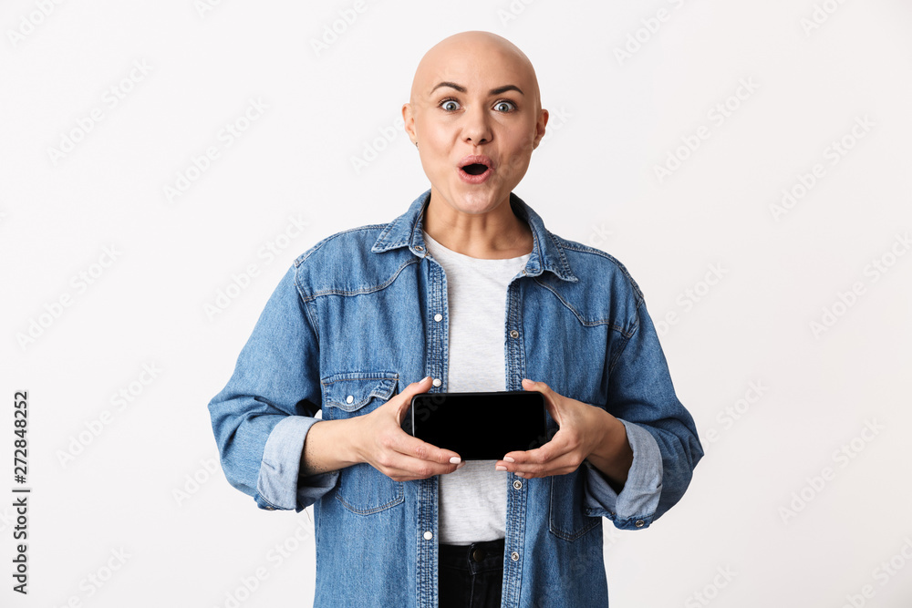 Bald woman posing isolated over white wall background showing display of mobile phone. Bald woman posing isolated over white wall background showing display of mobile phone.
