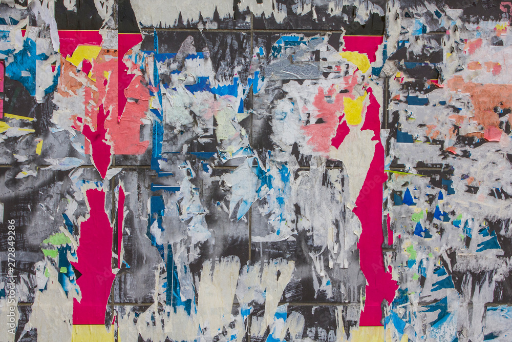 Fototapeta premium old dirty gray wall with multi-colored torn pieces of ads of different shapes and sizes. rough surface texture