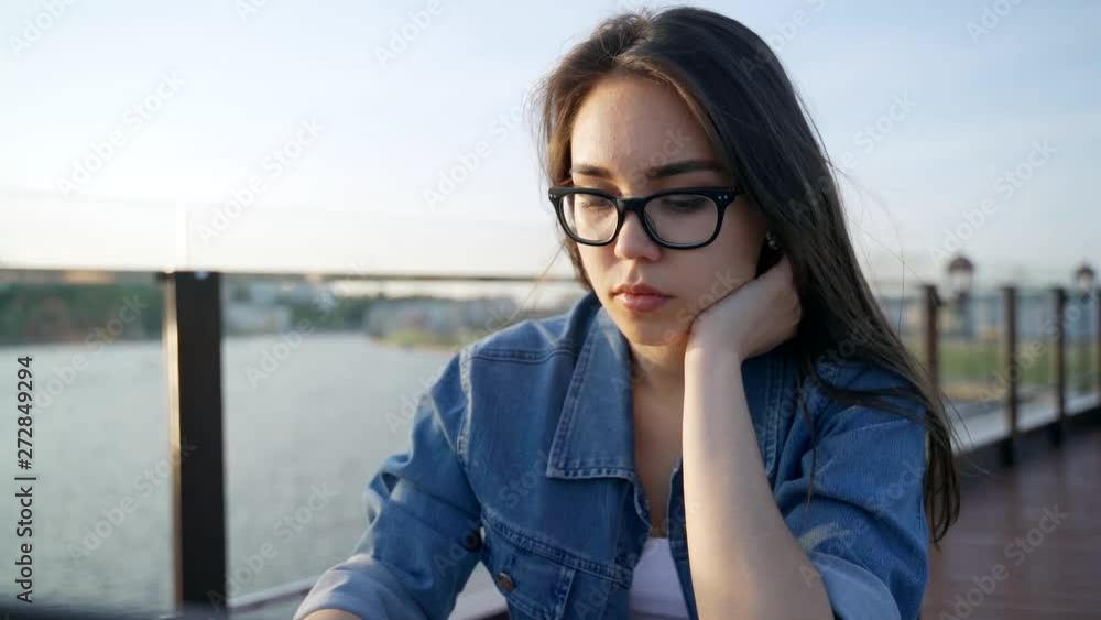 Beautiful young woman in glasses works on a laptop in an outdoor cafe Beautiful young woman in glasses works on a laptop in an outdoor cafe