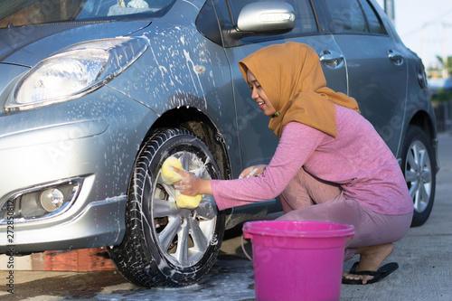 hijab woman cleaning car tires at outdoors area © SVRSLYIMAGES