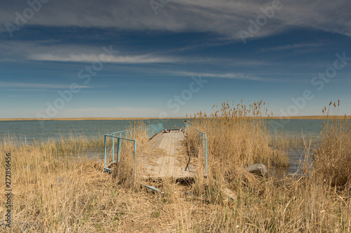 Old boat pier on the shore of the small Aral sea in Kazakhstan. In the foreground is tall grass.