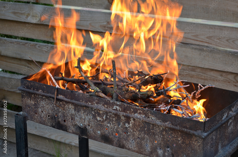 Dry wood for grilling burn with a large flame on the grill, on a background of a wooden fence, closeup