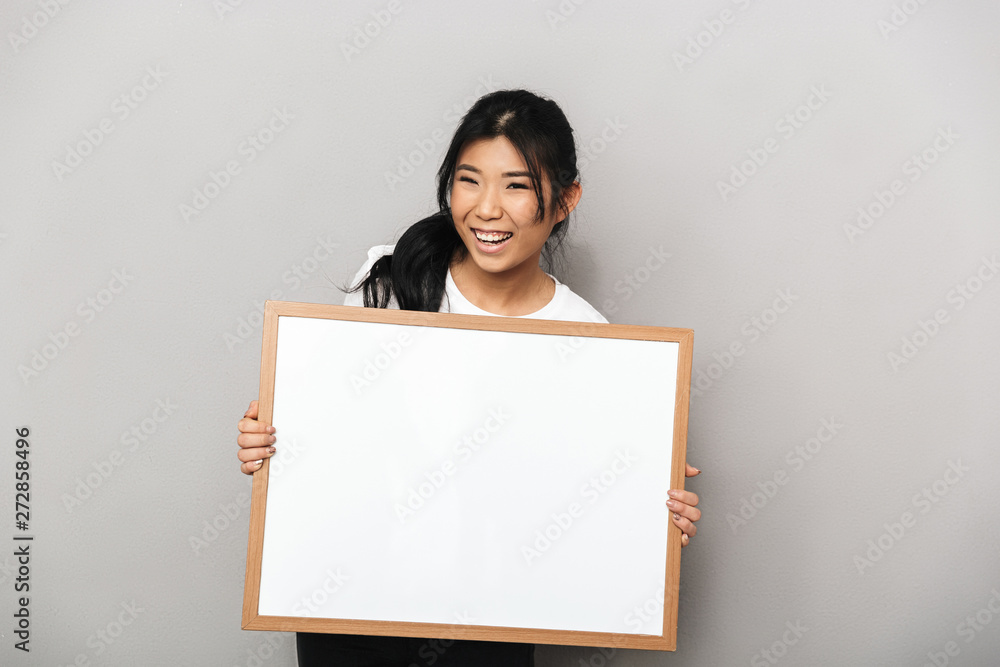 Asian beautiful young woman posing isolated over grey wall background holding blank copyspace. Asian beautiful young woman posing isolated over grey wall background holding blank copyspace.
