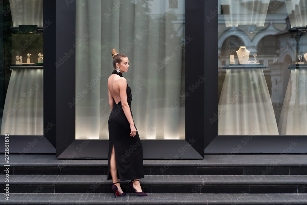 Beautiful girl in a long black dress posing in full growth near the boutique. Graceful interesting poses. Beautiful girl in a long black dress posing in full growth near the boutique. Graceful interesting poses.