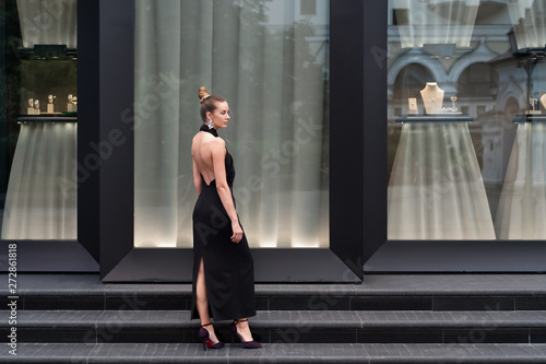 Beautiful girl in a long black dress posing in full growth near the boutique. Graceful interesting poses. © Денис Бухлаев
