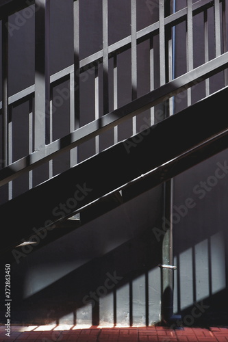 Sunlight and shadow on surface of black metal staircase with banister and concrete wall background outside of building in dark tone style and vertical frame, exterior architecture concept