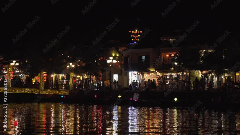 People walking in Hoi An, Vietnam at night on the street beside the river and crossing the bridge People walking in Hoi An, Vietnam at night on the street beside the river and crossing the bridge