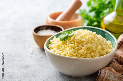 Cooked couscous with cilantro in ceramic bowl on concrete background. Selective focus. photo
