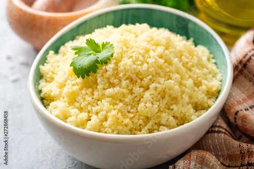 Cooked couscous with cilantro in ceramic bowl on concrete background. Selective focus.