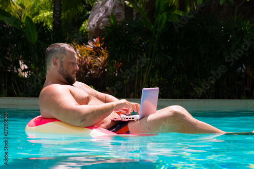 Male businessman with an inflatable ring in the water in the pool. Funny Fat Man in Swimming Circle with Pink Laptop. freelance concept.