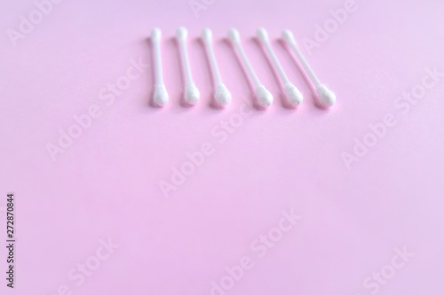 Row of white clean cotton swabs with selective focus on pink neutral background with empty space for text. Personal hygienic cotton buds for daily routine. Soft cotton ear sticks. Healthcare tools 