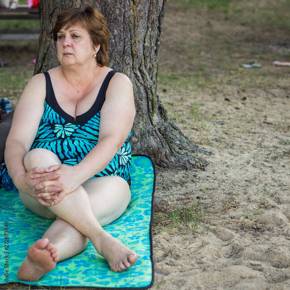 Mature woman resting on the beach by the lake. Mature woman resting on the beach by the lake.