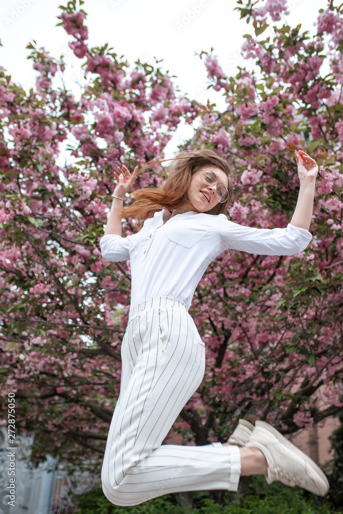 beautiful young happy woman in a blouse and glasses near the cherry blossoms. flowers beautiful young happy woman in a blouse and glasses near the cherry blossoms. flowers