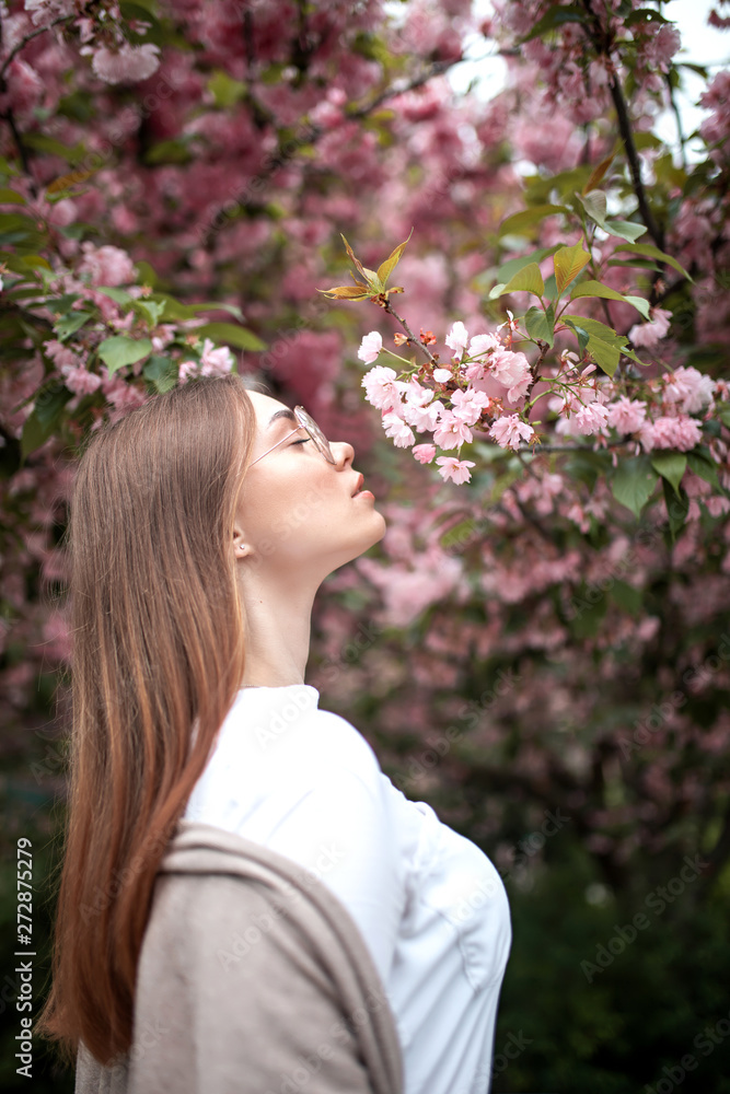 beautiful young happy woman in a blouse and glasses near the cherry blossoms. flowers beautiful young happy woman in a blouse and glasses near the cherry blossoms. flowers