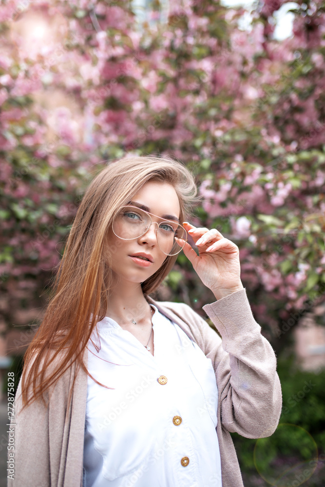 beautiful young happy woman in a blouse and glasses near the cherry blossoms. flowers beautiful young happy woman in a blouse and glasses near the cherry blossoms. flowers