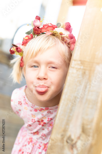 süßes blondes Mädchen mit Blumenkranz steckt Zunge raus 