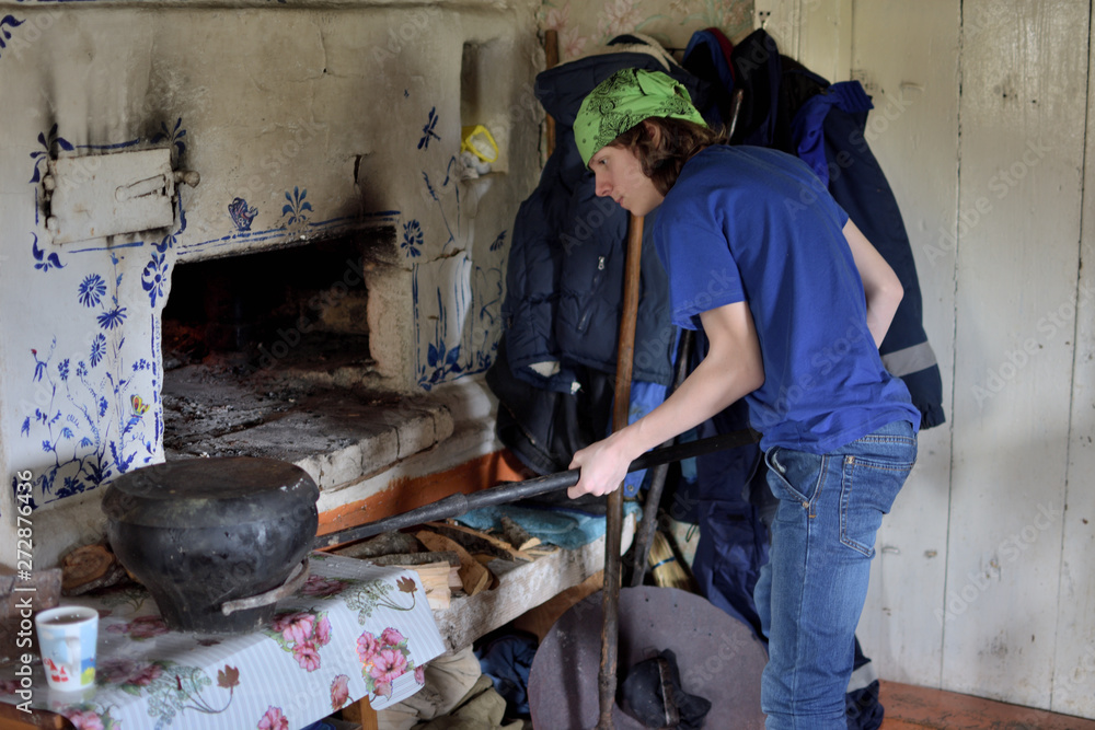teenage boy putting a heavy pot into russian stove with a grip teenage boy putting a heavy pot into russian stove with a grip
