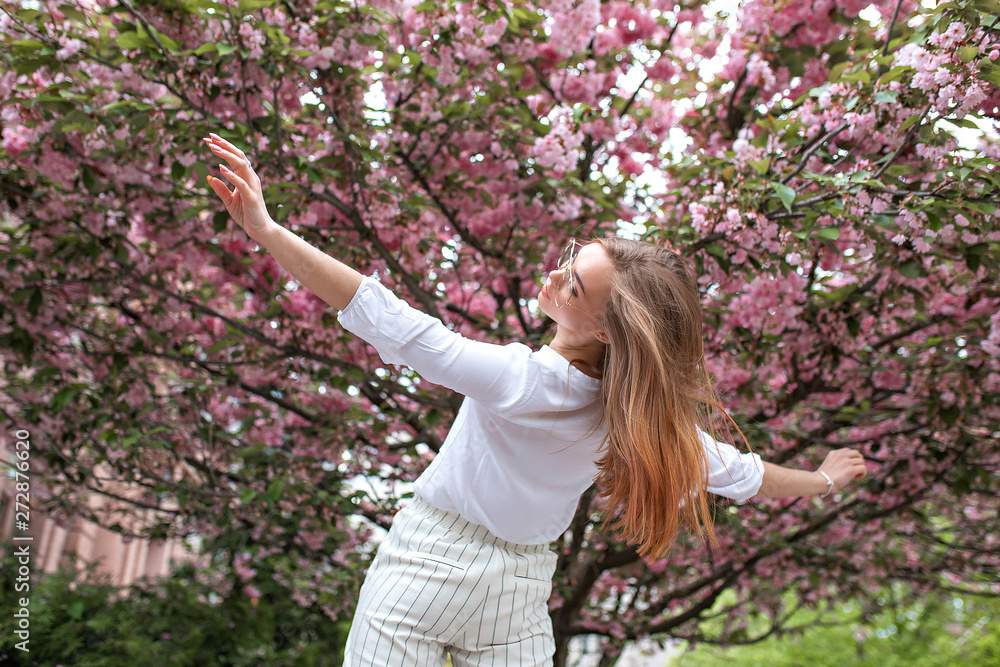 beautiful young happy woman in a blouse and glasses near the cherry blossoms. flowers beautiful young happy woman in a blouse and glasses near the cherry blossoms. flowers