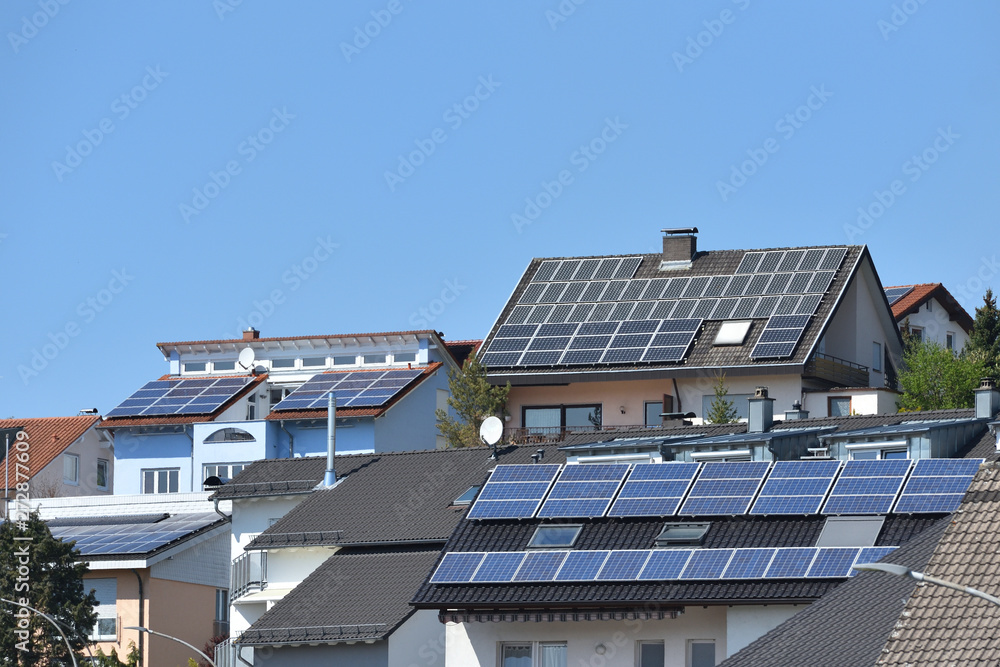 Several roofs of houses with solar panels under the blue sky. Solar panels on roofs with tiles Several roofs of houses with solar panels under the blue sky. Solar panels on roofs with tiles