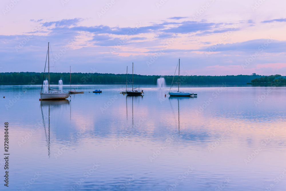 Peaceful landscape with sailboats moored on the lake  under rhe blue cloudy sky at sunset. Reflection of boats and clouds in water.