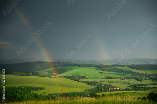 Summer landscape after storm, rainbow and green meadow