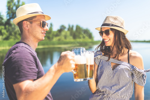 Beautiful couple cheering with beer glasses in nature. Summer vacation and party concept.