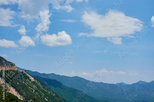 paraglider flying against the backdrop of mountains and clouds on a sunny day.