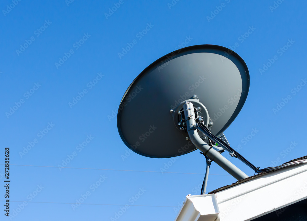 Satellite dish mounted to residential rooftop. with blue sky backdrop.