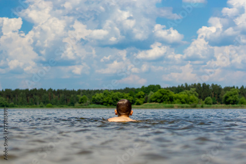 The boy swims on the lake, rear view