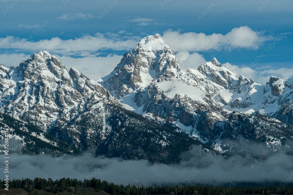Snow covered rocky mountain peaks with dramatic clouds and blue sky