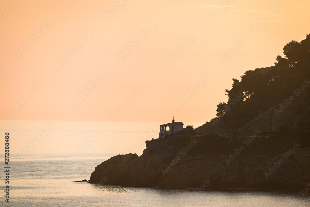 Beautiful sunset over Mediterranean sea. The small chapel on the forest-covered rocks. Madonnina della Punta, Bonassola, Liguria, Italy