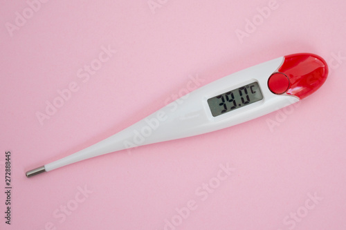 White digital clinical thermometer on pink background shows fever heat