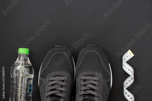 Fitness flat lay. Healthy lifestyle and sport concept. Black sneakers, tape measure and bottle of water on a black background.