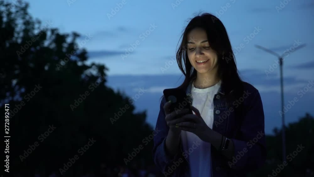 beautiful brenette womanl with smartphone on the low-light street in the park in the evening beautiful brenette womanl with smartphone on the low-light street in the park in the evening