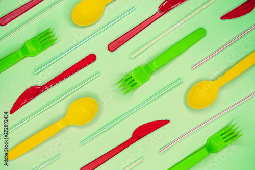 Multicolored plastic disposable forks, spoons. knives and straws on light blue background.