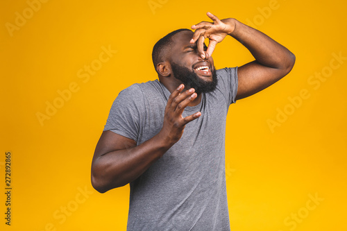 Afro american man isolated against yellow background smelling something stinky and disgusting, intolerable smell, holding breath with fingers on nose. Bad smells concept. photo